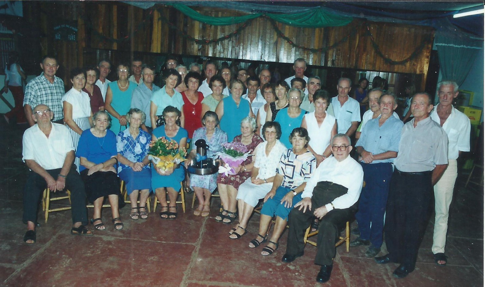 Grupo de idosos da comunidade reunido com flores num salão, 2003