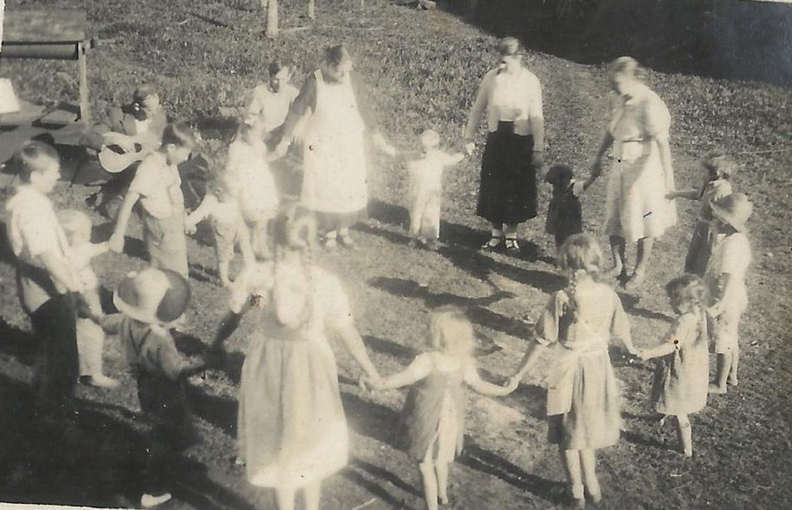 Crianças e adultos em grande roda de brincadeira num gramado, c.1940