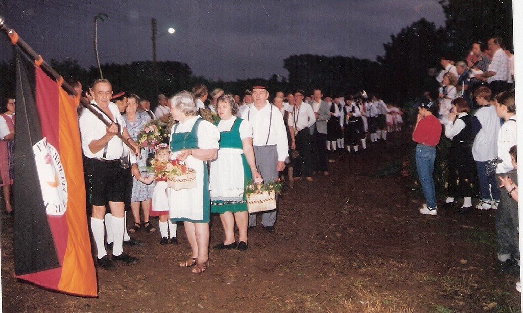 Desfile noturno com a bandeira da Alemanha e grupo em trajes típicos