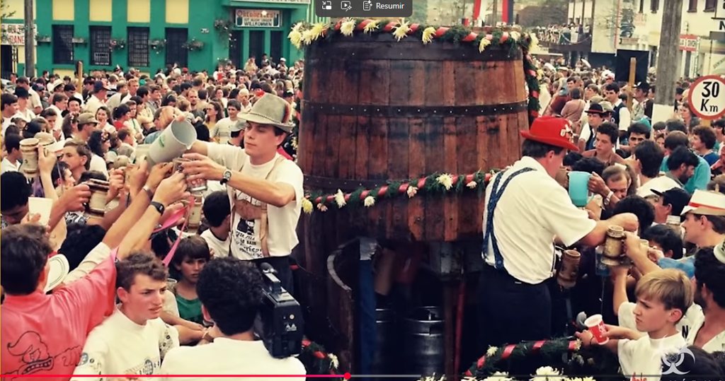 Multidão brindando com canecas diante de um grande barril de chope na rua