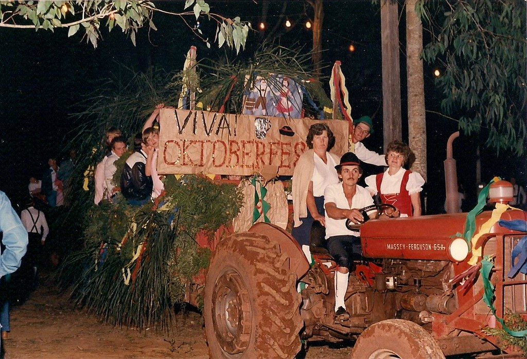 Trator enfeitado com a faixa "Viva Oktoberfest" e pessoas em trajes típicos