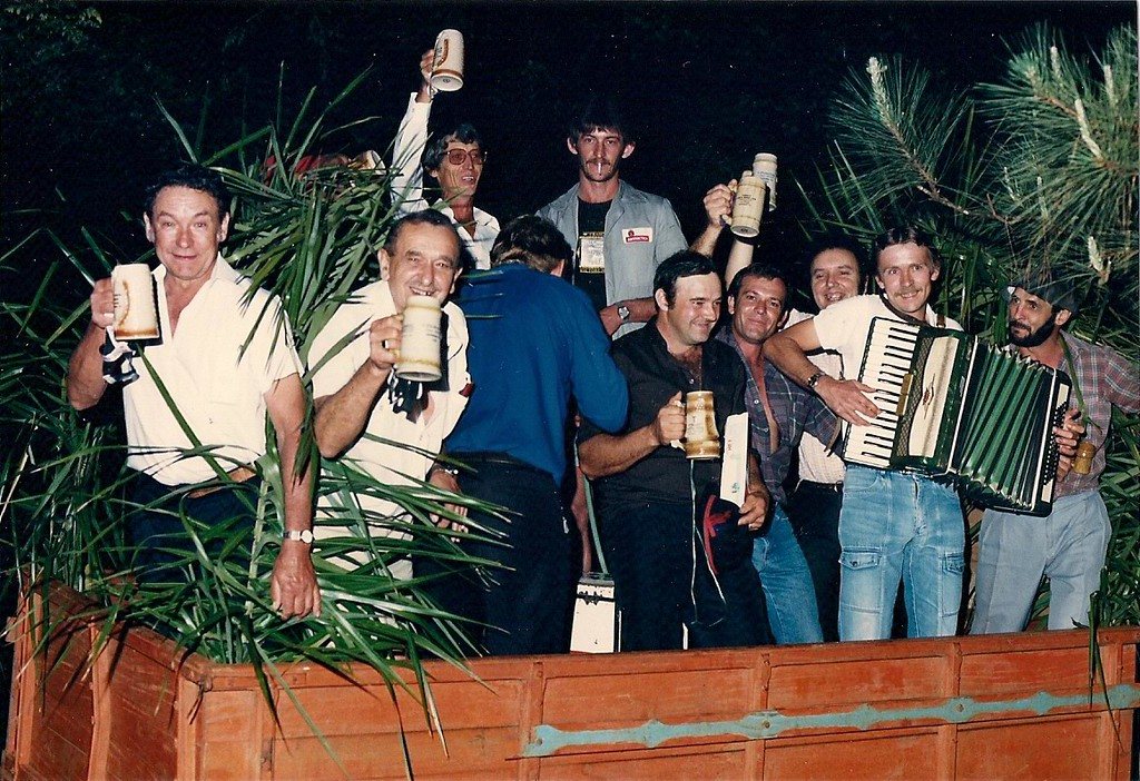 Rapazes na carroça do desfile brindando, com gaiteiro