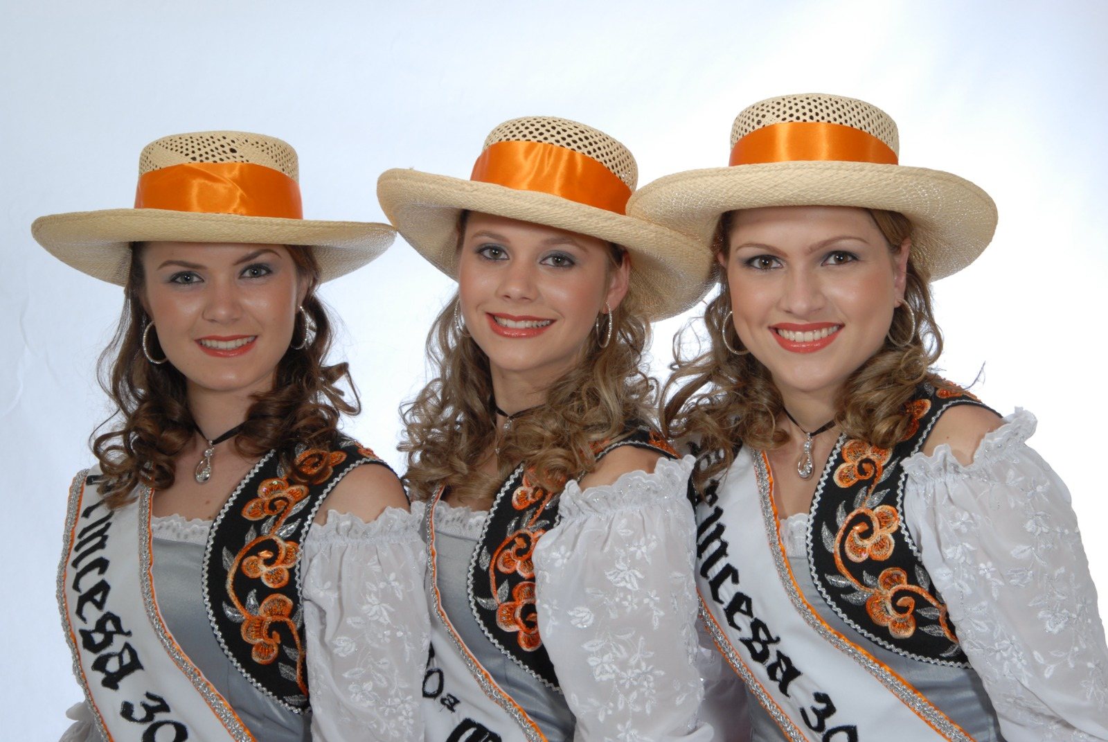 Três soberanas com chapéus de palha e faixas da 30ª Oktoberfest